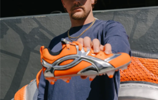 Gunnar Henderson holds new Under Armour cleat next to 10 foot life-size Under Armour Cleat in Home Run Porch at Camden Yards