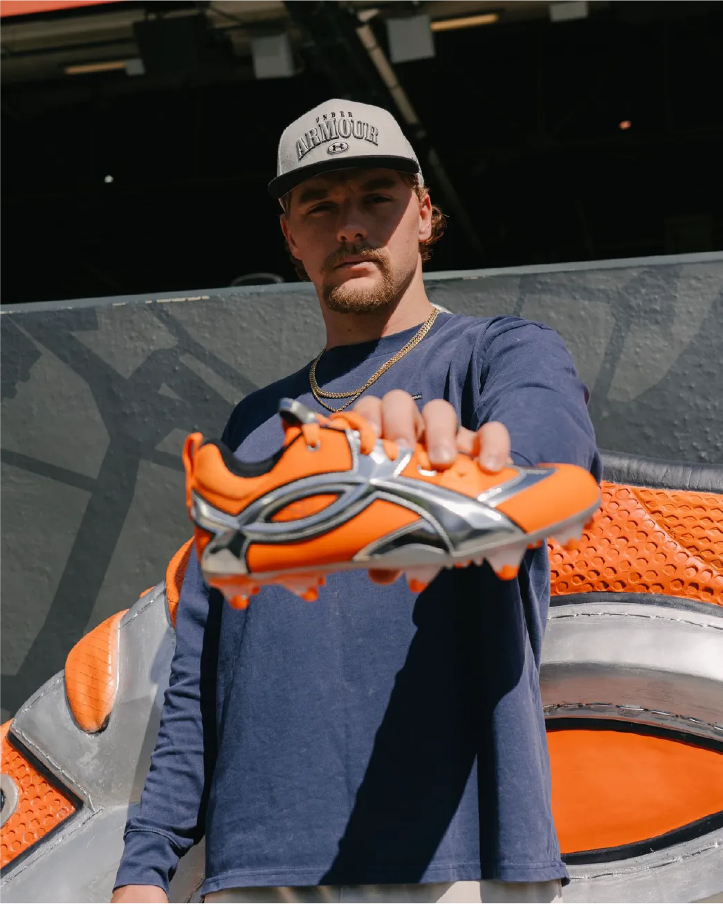 Gunnar Henderson holds new Under Armour cleat next to 10 foot life-size Under Armour Cleat in Home Run Porch at Camden Yards