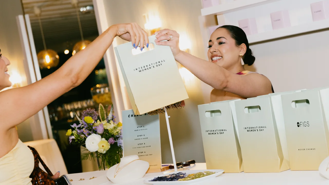 A woman gives a bag to an attendee for a FIGS event celebrating International Women's Day at kiosk built by Fuller Street and their experiential fabrication team in Los Angeles